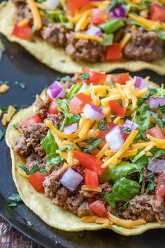 two tortillas topped with meat, cheese and veggies on a black plate