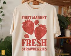 "Fruit Market Fresh Strawberries" Unisex T-shirt Design by jojoyu This item is made to order. If you want an oversized fit please size up! for reference, the model on the photo is usually a medium but wearing XL for an oversized fit. About the shirt: ◦ color: ivory ◦ relaxed fit  ◦ soft-washed, garment-dyed fabric ◦ double-needle stitching throughout the tee makes it highly durable  ◦ made with medium fabric (6.1 oz/yd²) consisting of high quality, 100% ring-spun US cotton for long-lasting comfo Fruit Graphic Tee, Strawberry Merch, Strawberry Clothes, Strawberry Tshirt, Strawberry Aesthetic, Retro Cottage, Fruit Shirt, Strawberry Shirt, Fruit Market