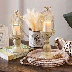 two candles are sitting on a table next to a birdcage with feathers in it