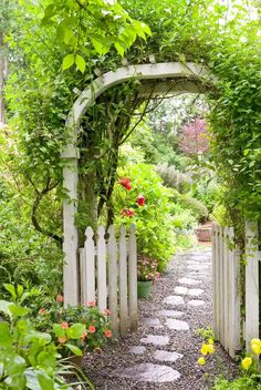 a garden with a white fence and flowers on the side, surrounded by greenery