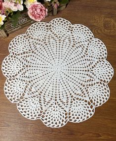 a white doily sitting on top of a wooden table next to pink and yellow flowers