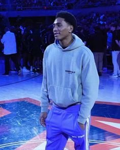 a man standing on top of a basketball court wearing purple sweatpants and a hoodie