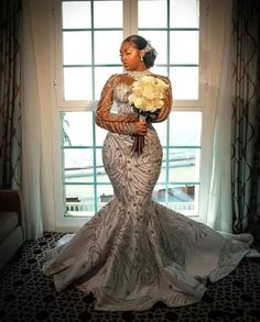 a woman standing in front of a window holding a bouquet of flowers and wearing a dress