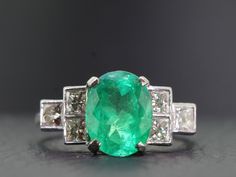 A beautifully  proportioned, bright and vibrant Colombian Emerald is the focal point of this sophisticated and artfully sculpted Gold and Diamond ring. This stunning ring boosts an oval 2.35 carat Colombian Emerald which is flanked by bright white high premium six princess cut sparkling Diamonds, totaling one carat. Quality;  H Colour,  Clarity:  VS1  The Diamonds sparkle and glisten with immense lustre. The Colombian Emerald is set in a secure classic four prong setting and displays a hue of li Art Deco Oval Emerald Ring With Brilliant Cut, Oval Hallmarked Emerald Ring In Platinum, Hallmarked Oval Emerald Ring In Platinum, White Gold Oval Emerald Ring Art Deco Style, Exquisite Oval Emerald Ring In Platinum, Oval Emerald Ring With Diamond Cut In Platinum, Gia Certified Oval Emerald Ring In Art Deco Style, Art Deco Oval Diamond Ring With Vvs Clarity, Luxury Oval Emerald Ring With Brilliant Cut