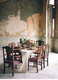 a dining room table set for four with flowers on the table and chairs around it