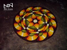 a circular rug with an orange and green design on it's side in the middle of a floor