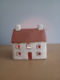 a small ceramic house sitting on top of a wooden table next to a white wall