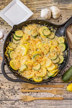 an iron skillet filled with zucchini and cheese on top of a wooden table