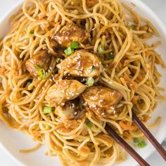 a white plate topped with noodles and meat covered in gravy next to chopsticks