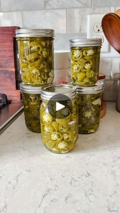 four jars filled with pickles sitting on top of a counter