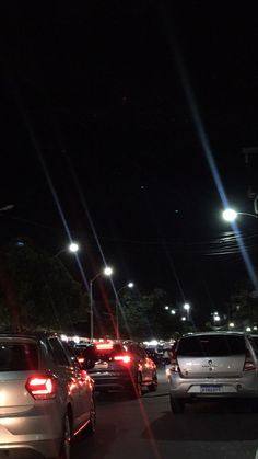 many cars are parked on the side of the road at night with street lights in the background