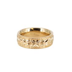 a gold wedding ring with leaves on the side and engraving in the middle, set against a white background