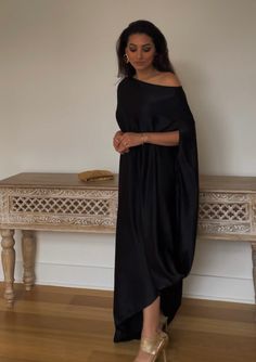 Introducing the Devan Kaftan Gown – a timelessly elegant piece crafted from black satin, featuring a off-shoulder design with a drape to flatter the silhouette. Accented with hand-bead work on the shoulder and an optional belt for a cinched-in waist, the dress offers an ethereal, effortless style that will make a statement. Perfect for any luxurious event. Features: off-shoulder design hand work embellishments on the shoulder comes with an optional belt Included in purchase: Devan Gown, Belt Black One-shoulder Dress With Draped Sleeves, Black Maxi Dress With Draped Sleeves, Black Satin Off-shoulder Dress, Chic Silk Off-shoulder Evening Dress, Elegant Black Off-shoulder Dress For Wedding, Elegant Black Off Shoulder Dress For Wedding, Black Dress With Draped Sleeves And Asymmetrical Neckline, Black Satin Dress With Draped Sleeves, Silk Off-shoulder Maxi Dress For Cocktail