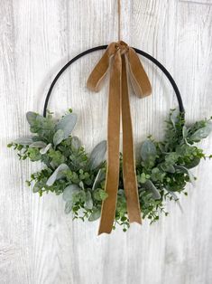 a wreath with greenery and ribbon hanging on a white wooden wall in the shape of a circle