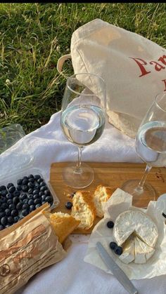 wine, cheese and blueberries are on a picnic blanket in the grass next to some bread