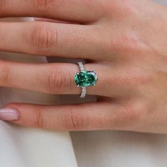 a woman's hand wearing a ring with a green stone in the center and diamond band