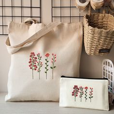 two bags with embroidered flowers on them next to a basket and some yarn spools