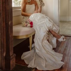 a woman in a wedding dress sitting on a bench next to a window with flowers