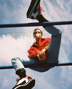 a woman sitting on top of a metal pole next to another person wearing black sneakers