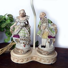 two figurines are sitting on a table next to a lamp and potted plant