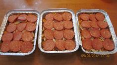 three tin pans filled with hot dogs on top of a wooden table