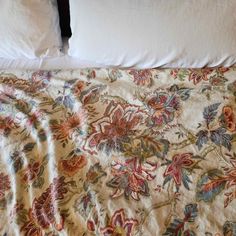 an unmade bed with white pillows and floral bedspread