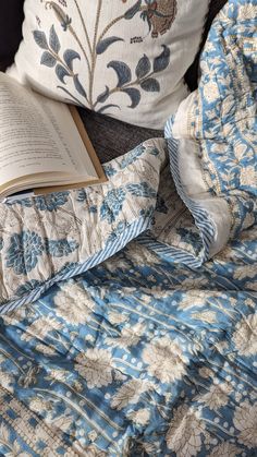 an open book laying on top of a blue and white comforter next to a pillow