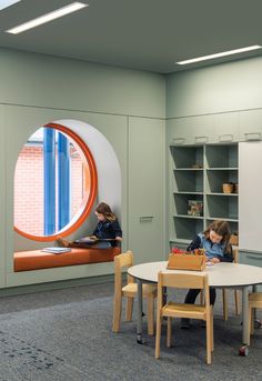 two children are sitting at a table in an office with bookshelves and cabinets