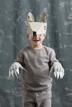 a young boy wearing a paper wolf mask and gray sweatpants, with his hands in the air