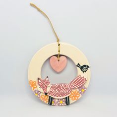 a wooden ornament with a pink fox and heart hanging from it's side