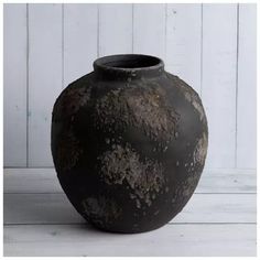 a large black vase sitting on top of a white wooden floor next to a wall