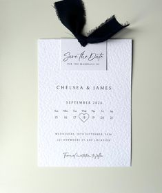 a wedding save the date card with a black ribbon tied to it's back