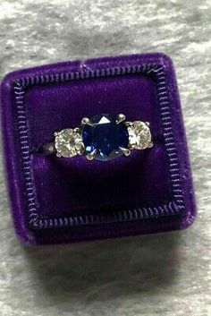 a purple ring with three stones in it sitting on top of a purple velvet box