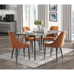 a dining room table with orange chairs and a rug on the floor in front of it