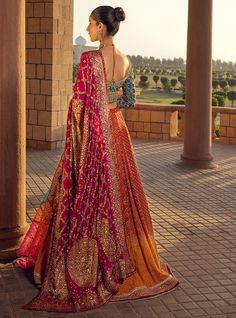 a woman standing in front of a couch wearing a red and gold bridal gown