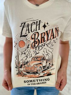 "Get ready to hit the road with the PLUS Zach Bryan Truck Tee! Featuring lyrics from his hit song "Something in the Orange", this cream graphic tee will add a touch of western charm to any outfit. Its short sleeves and crew neck make it perfect for any adventure. Yeehaw!" Cream Graphic Tee, Something In The Orange, Small Business Signs, Zach Bryan, Hit The Road, Glitz And Glam, Hit Songs, The Road, Graphic Tee