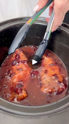 someone using tongs to stir food in a slow cooker with meat and sauce