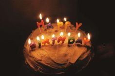 a birthday cake with lit candles that spell out the word, happy birthday on it