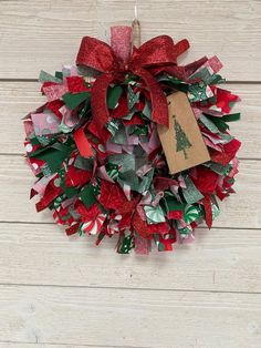 a red and green christmas wreath with a tag on it hanging on a wooden wall