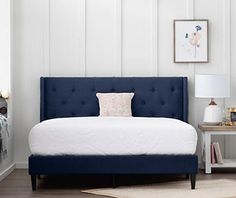 a blue bed with white sheets and pillows in a room next to a lamp on a table