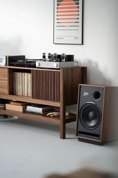 a record player sitting on top of a wooden shelf next to a speaker and bookshelf