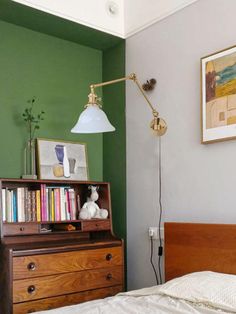 a bedroom with green walls and a wooden dresser in the foreground, an old fashioned lamp on the far wall