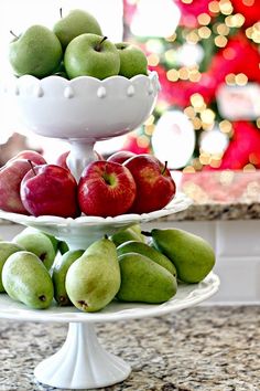 two tiered plates filled with apples and pears on a kitchen counter next to a christmas tree