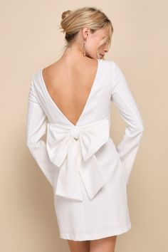 the back of a woman wearing a white dress with a bow at the waist and long sleeves