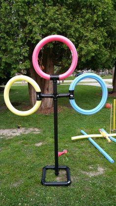 an outdoor sculpture made out of plastic rings and sticks in the grass with trees in the background