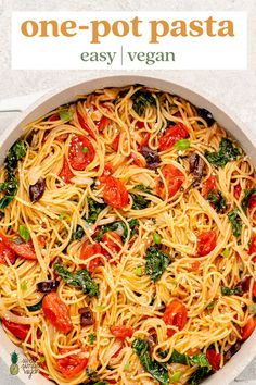 pasta with tomatoes, spinach and olives in a skillet on a white surface