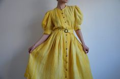 Vintage rustic yellow linen folk dress with puff sleeves, from the 1980s era Women's linen peasant dress with in shades of yellow, mid calf length, short puffy sleeves with pleats on the cuffs, buttoned front with gold plastic buttons, high waist and two pockets. The dress has a detachable belt and lining on the skirt. Made in Austria Material - 100% Linen, just the lining is synthetic Size on tag - 40 (EU) Model wears 38 EU or 8 US, fits slightly big in the bust area.  Approximate Measurements Vintage Linen Dress For Spring, Spring Vintage Linen Dress, Vintage Linen Dress For Spring Daywear, Summer Daywear Vintage Dress With Puff Sleeves, Summer Vintage Puff Sleeve Dress For Daywear, Vintage Linen Summer Dress, Fitted Linen Prairie Dress For Summer, Vintage Yellow Puff Sleeve Dress, Yellow Vintage Summer Dress For Daywear