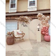 an arch made out of balloons is in front of a house with a chair and table