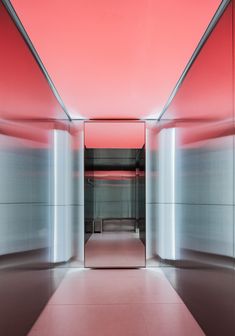 an empty hallway with pink walls and flooring in the center is lit by red lighting