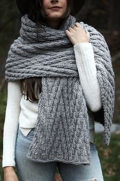 a woman wearing a gray knitted scarf with a black hat and white sweater on